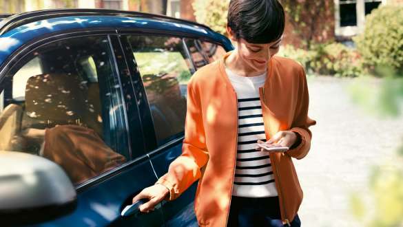 BMW TeleServices BMW TeleServices, mujer con smartphone junto a la puerta de un BMW