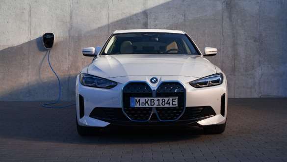 Vista del frontal con BMW Wallbox BMW i4 eDrive40 G26 2021 BMW i4 eDrive40 G26 2021 Mineralweiss, vista del frontal, delante de la pared de una casa con punto de carga BMW Wallbox