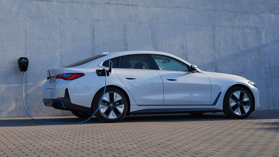Vista lateral con BMW Wallbox BMW i4 eDrive40 G26 2021 BMW i4 eDrive40 G26 2021 Mineralweiss, vista lateral delante del muro de una casa con un punto de carga BMW Wallbox