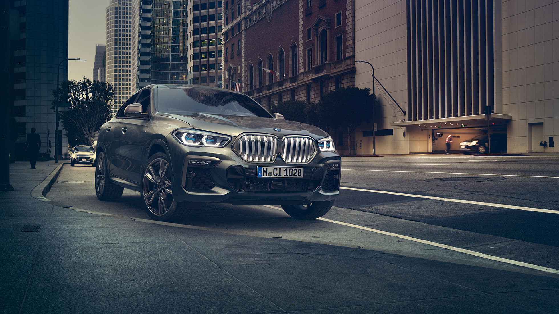 BMW X6 M50i parado BMW X6 M50i en perspectiva frontal de tres cuartos parado frente a un escenario urbano.