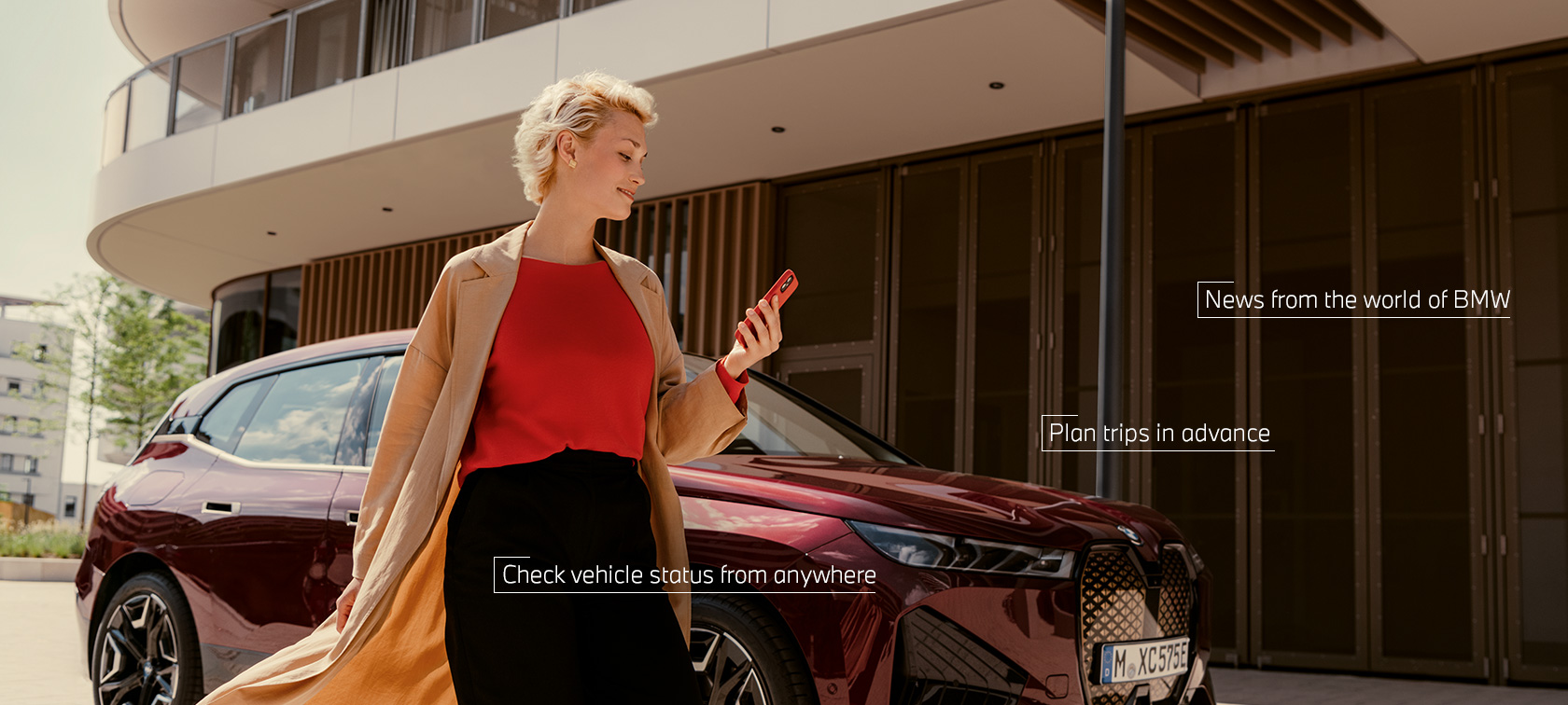 Una mujer de pie delante de un BMW X5 blanco utiliza My BMW App en el smartphone Una mujer de pie delante de un BMW X5 blanco utiliza My BMW App en el smartphone